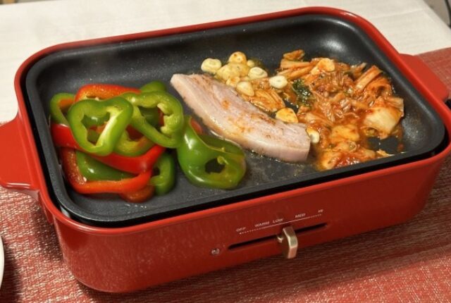 赤いホットプレートで肉とピーマンを焼いている