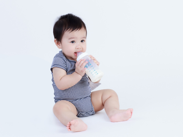 哺乳瓶を咥えながらお座りしている赤ちゃん