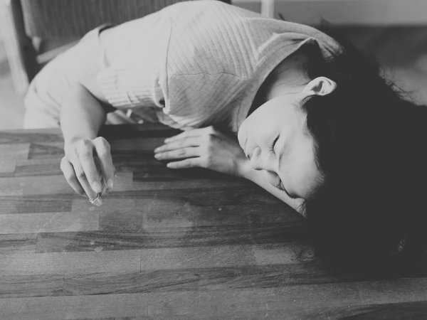 白黒画像、机に突っ伏して目を閉じている女性