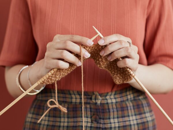 棒針編みをしているオレンジ色の服を着ている女性