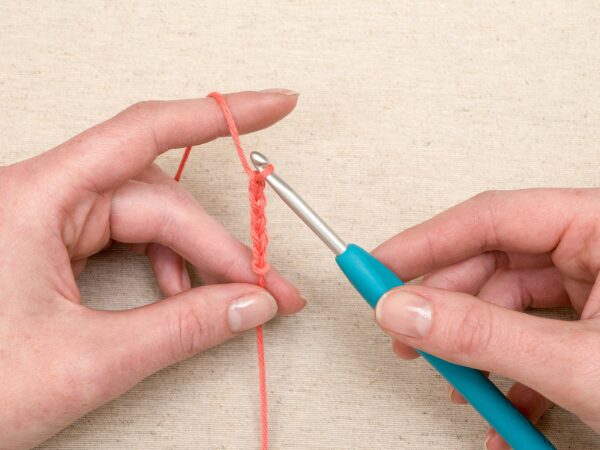 水色のかぎ針でオレンジ色の毛糸のくさり編みをする手