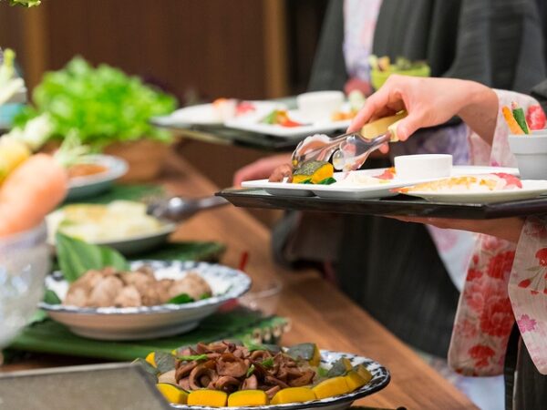 ビュッフェでトングでおかずを取っている女性の手