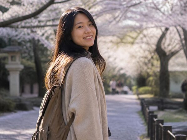 桜並木を背景にこちらを向いて笑顔のリュックを背負った女性