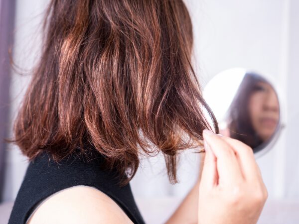 乾燥した髪の毛を手鏡で見ている女性